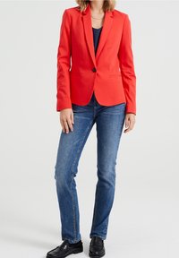 Red blazer with a structured design, single button closure, and notched lapels. Paired with fitted blue jeans and black loafers.