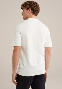 Fehér, rövid ujjú pólóing, textúrált kötött anyagból, bordázott gallérral és mandzsettával, egyenes aljjal. Sötét nadrággal viselve, hátulról nézve.