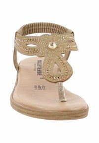 Sandalo piatto beige con cinturino decorativo intagliato, dotato di borchie metalliche e un accento di gioiello al centro. Suola flessibile e soletta imbottita.