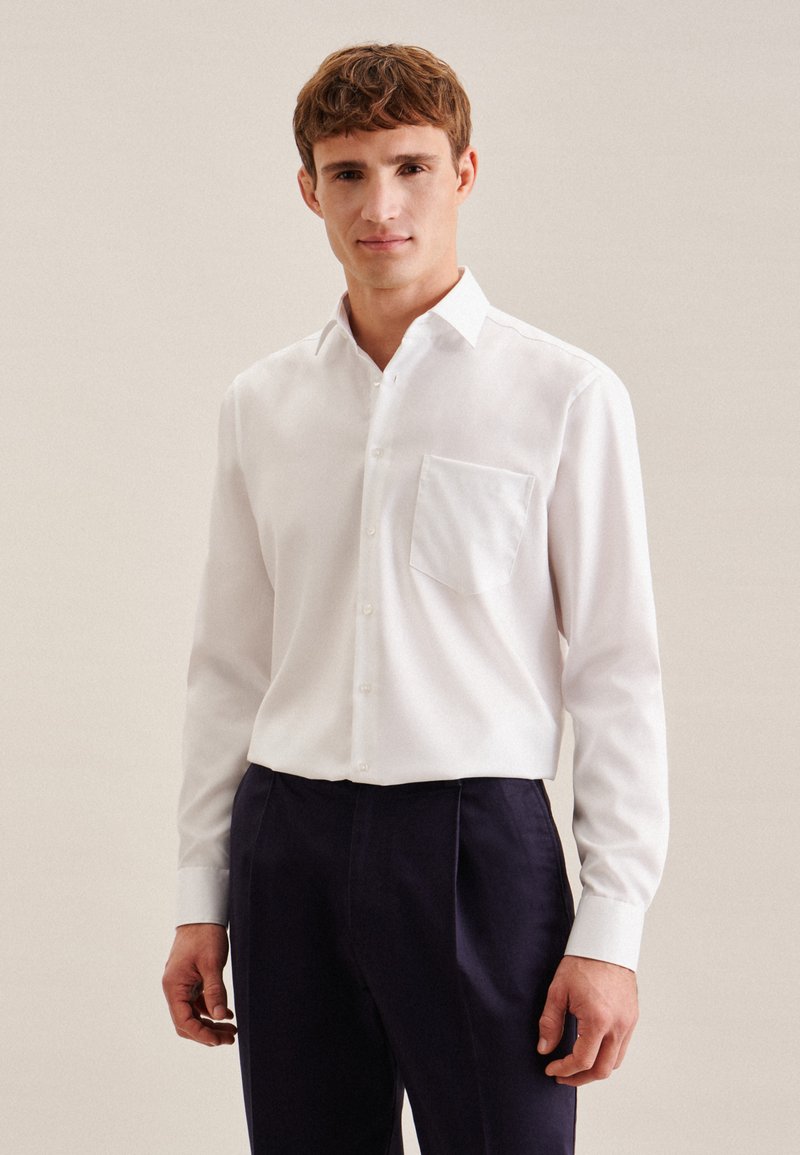 Chemise blanche à boutons, avec une poche poitrine, des manches longues et un col classique, assortie à un pantalon bleu marine foncé. Texture lisse.