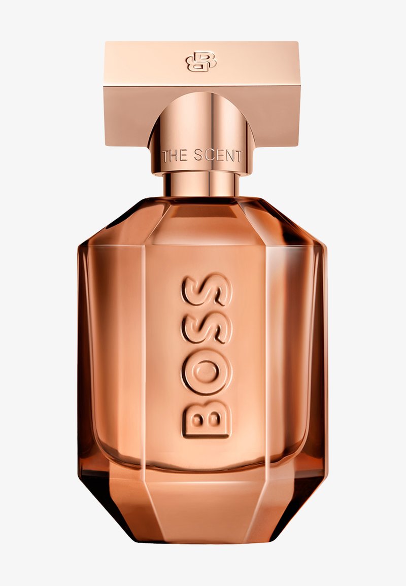 Flacon de parfum en verre facetté couleur or rose avec "BOSS" embossé verticalement et un bouchon rectangulaire gravé des initiales "BOSS".