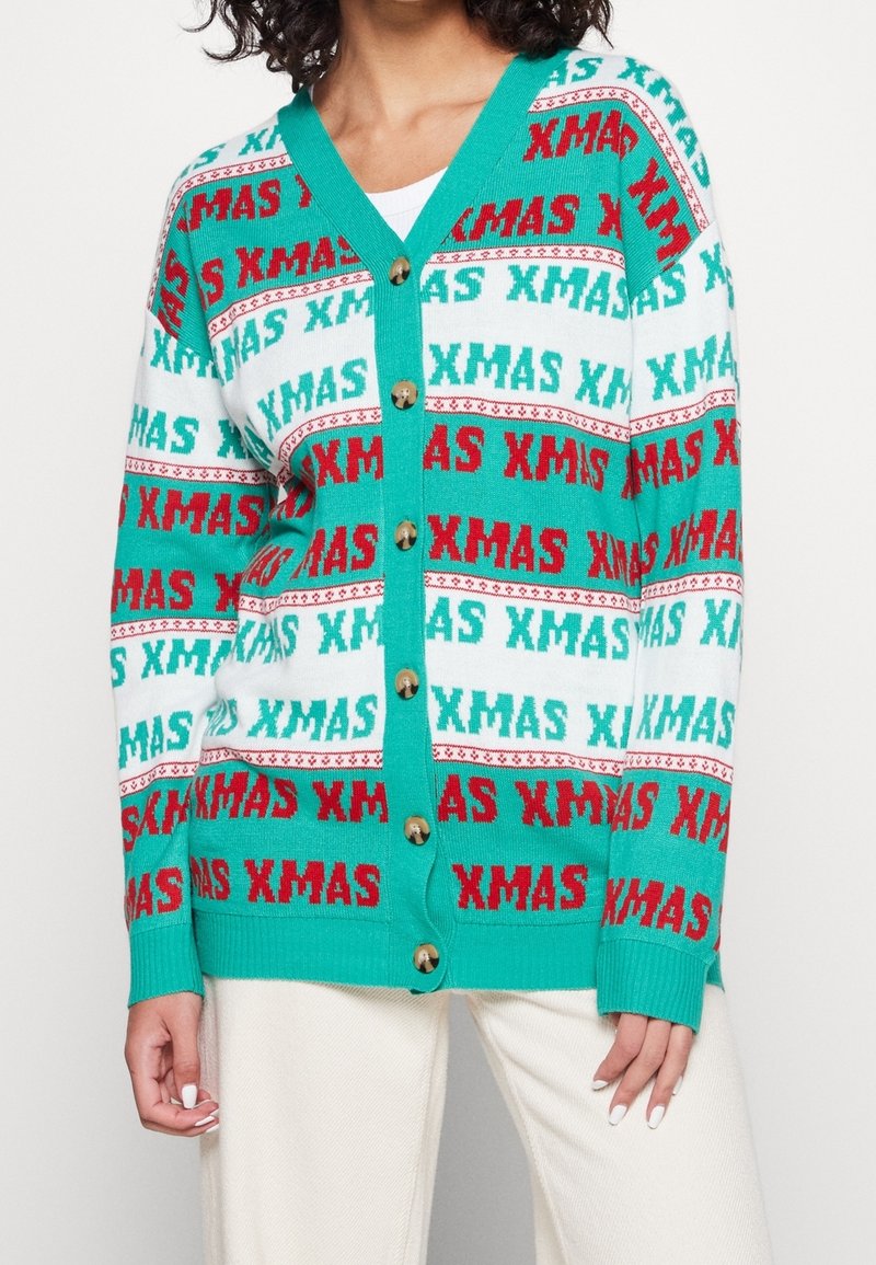 Dzianinowy kardigan z turkusowym tłem, ozdobiony powtarzającym się wzorem tekstu "XMAS" w kolorze czerwonym i zielonym, wykończony złotymi guzikami.