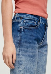 Spijkerbroek van denim met een vervaagde blauw-wastint, vijf-pocket ontwerp en zichtbare stiksels. Het materiaal lijkt zacht met een lichte rek.