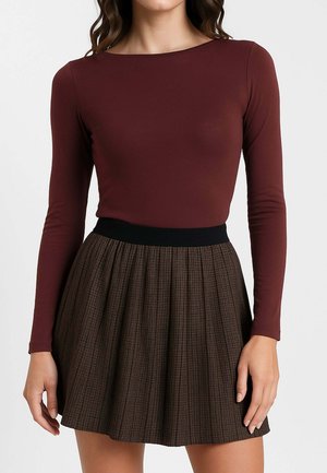 Donna che indossa un top bordeaux attillato a maniche lunghe infilato in una gonna a pieghe marrone a quadri con una vita alta e un cinturino nero.