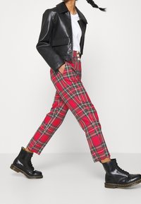 Svart fusk läderkort jacka, vit t-shirt, röda rutiga byxor och svarta snörstövlar. Anmärkningsvärda guldknappar på byxorna.