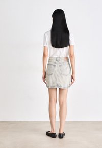 Denimrok in een licht gewassen kleur, boven de knie, met een aansluitende taille, achterzakken en een gestikte zoom. Gecombineerd met een wit T-shirt en zwarte ballerina's.