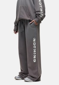 Grijze oversized hoodie met een buidelzak aan de voorkant en grafische opdruk op de mouwen, gecombineerd met grijze sweatpants met zijgraphics.