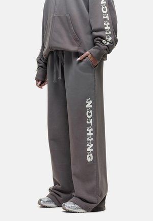 Grijze oversized hoodie met een buidelzak aan de voorkant en grafische opdruk op de mouwen, gecombineerd met grijze sweatpants met zijgraphics.