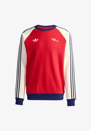 Czerwona bluza z kapturem z białymi i granatowymi akcentami, posiadająca okrągły dekolt, długie rękawy oraz trzy paski na każdym rękawie. Na piersi znajdują się logotypy.