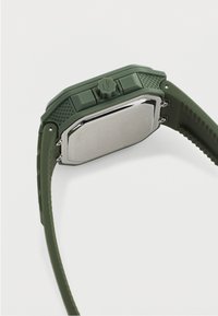 Πράσινο ψηφιακό ρολόι με υφασμένες πλευρές, μεταλλική πλάτη και ρυθμιζόμενο λουράκι με ραβδώσεις σε λευκό φόντο.