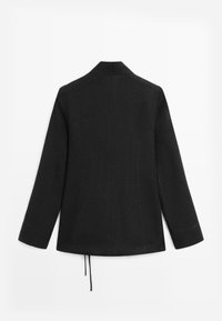 Blazer noir sur mesure avec manches longues, coutures arrière pour la mise en forme et un cordon suspendu à l'ourlet inférieur arrière.