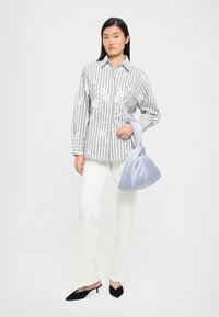Chemise à rayures avec broderies florales, associée à un pantalon blanc et un sac en satin bleu doux. Des chaussures noires à enfiler à bout pointu complètent le look.