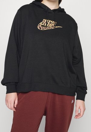 Personne portant un sweat à capuche noir ample avec un logo Nike imprimé léopard et un pantalon de survêtement bordeaux avec un petit logo Nike blanc.
