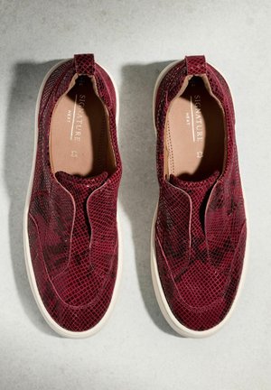 Een paar bordeauxrode instapsneakers met een textuurpatroon en witte zolen, op een lichtgrijze achtergrond geplaatst, gezien van bovenaf.