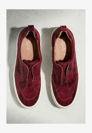 Een paar bordeauxrode instapsneakers met een textuurpatroon en witte zolen, op een lichtgrijze achtergrond geplaatst, gezien van bovenaf.