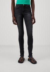 Svarta smala jeans med fransad fåll, tillverkade av denimtyg. Matchas med svarta flip-flops med en tjock sula och remdesign.