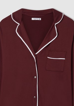 Maglietta da pigiama bordeaux con piping bianco, chiusura con bottoni e taschino sul petto. Realizzata in materiale morbido, presenta un design classico con colletto.