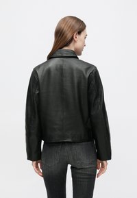 Μαύρο δερμάτινο μπουφάν με κλασικό γιακά, κοντό σχέδιο και μινιμαλιστικές λεπτομέρειες. Λείο υλικό με εμφανείς ραφές. Εμφανίζεται η πίσω όψη.