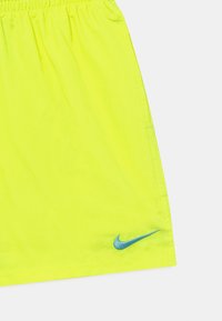 Pantalones cortos deportivos amarillos con una cinturilla elástica, que presentan un logo de Nike azul en la parte inferior derecha. Textura de tela suave y ligera.