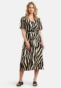 Zwart en crèmekleurig gestreepte wikkeljurk met korte mouwen, een ceintuur in de taille, en een rok van gemiddelde lengte, gecombineerd met zwarte blokhak sandalen.