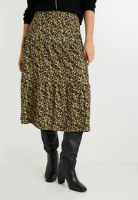 Falda midi floral en mostaza con patrón de flores en blanco y negro, con cintura elástica y diseño de volantes en capas.
