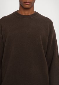 Dark brown ribbed knit sweater with a crew neckline and loose fit. The texture appears soft and thick, suitable for cooler weather.