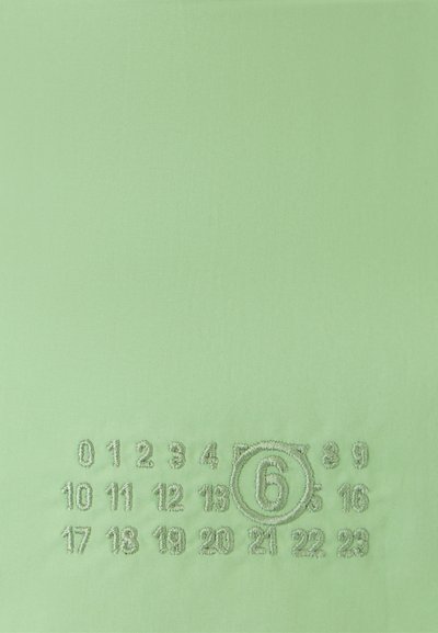 Šviesiai žalia medžiaga turi siuvinėtus numerius tinklelio raštu, išryškintas „6“ apskritime. Sklandus paviršius, minimalus dizainas.