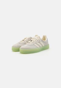 Light gray suede sneakers with green translucent soles, featuring three white stripes, round laces, and a smooth leather heel accent.