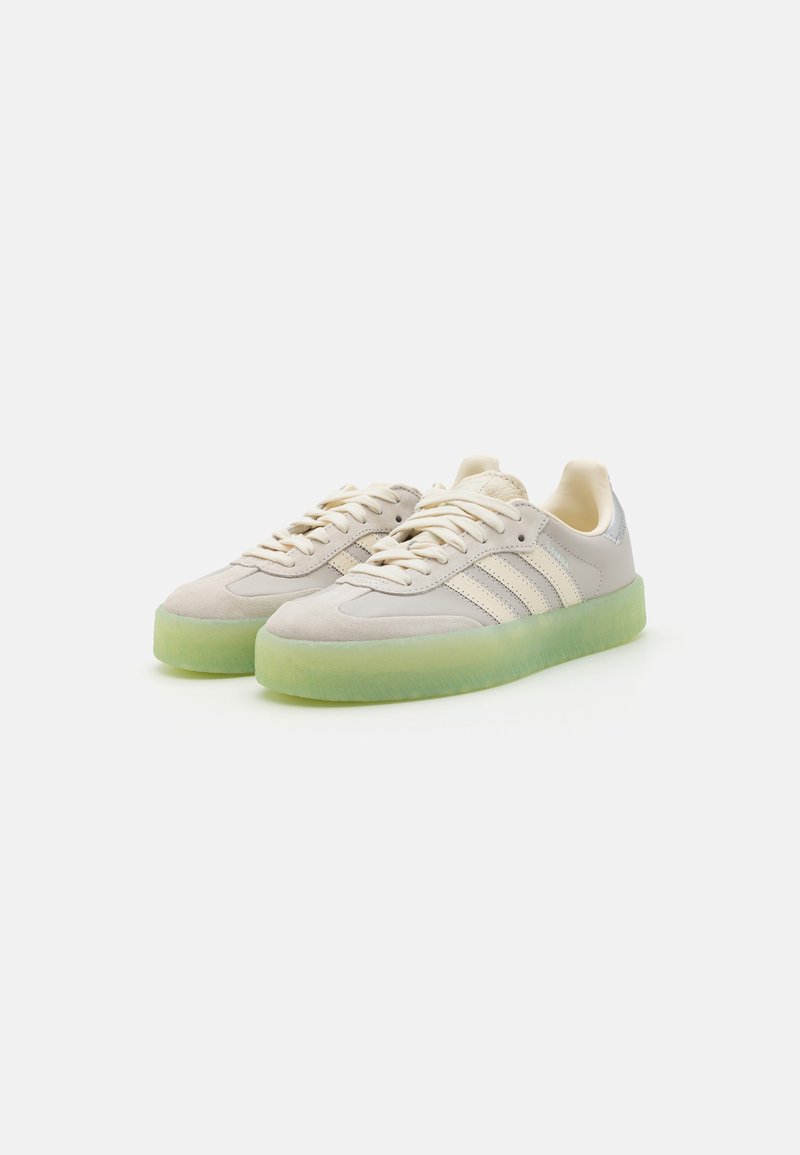 Sneakers in suede grigio chiaro con suole trasparenti verdi, caratterizzati da tre strisce bianche, lacci rotondi e un'accensione in pelle liscia sul tallone.