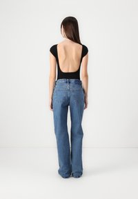Black bodysuit with a low back paired with high-waisted blue jeans, featuring a relaxed fit and large back pockets. Smooth fabric texture.