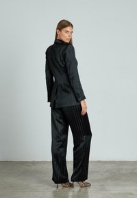 Completo a righe nere con giacca su misura e pantaloni a gamba larga, caratterizzato da accenti lucenti e una texture morbida. Vista posteriore mostrata.