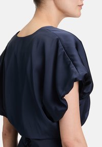 Nawigacyjna satynowa sukienka z szerokim, drapowanym dekoltem oraz krótkimi bufkami, z zebranym detalem z tyłu i gładką teksturą.