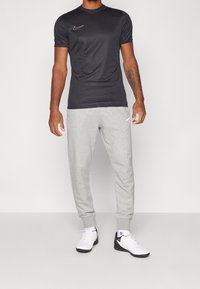 Schwarzes Sport-T-Shirt mit goldenem Nike-Logo, kombiniert mit grauen Sweatpants. Weiße Sneaker mit schwarzen Akzenten. Glattes Material und taillierte Form.