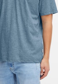 Niebieski melanżowy T-shirt z krótkim rękawem wykonany z miękkiego materiału, z luźnym krojem i małą metką na bocznym szwie.