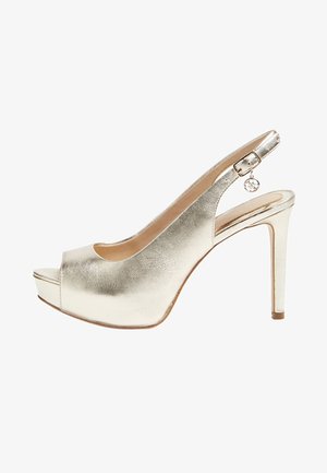 Zapato de tacón alto metálico dorado con punta abierta, talón descubierto, tacón delgado y una correa ajustable con hebilla que incluye un pequeño colgante.