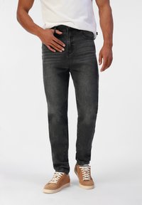 Jean en denim noir avec une coupe slim, dotés d'une taille mi-haute, de cinq poches et de détails légèrement décolorés, associés à des baskets en suède tan.