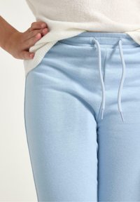 Hellblaue Sweatpants aus weichem Stoff, mit einem elastischen Bund und Kordelzug. Sanfte Textur und minimalistische Designdetails.