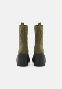 Botas de tela verdes hasta el tobillo con acabado liso, con punta cuadrada y tacones negros gruesos, diseñadas con lengüetas para facilitar su puesta.