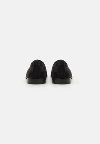 Mustad sametist loafers, millel on tekstureeritud muster, lame konts ja ümar nina. Tagantvaates on näha siledat õmblust ja läikivaid detaile.