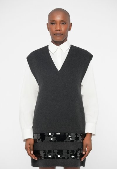 Grauer ärmelloser Pullover aus weichem Stoff, über ein weißes Hemd mit Kragen getragen. Mit einem V-Ausschnitt und einem strukturierten schwarzen Paillettenakzent am unteren Ende.