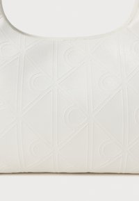 Geantă albă din material texturat, având un model geometric reliefat. Designul include linii diagonale și accente circulare.