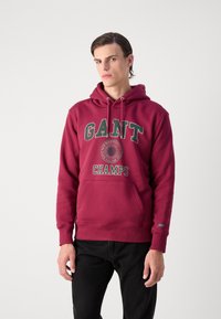 Felpa bordeaux con tasca a marsupio frontale, con la stampa di "GANT" e "CHAMPS" in verde e bianco. Tessuto misto cotone, design morbido e rilassato.