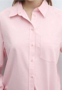 Helles rosa Hemd mit Knöpfen aus Baumwolle, mit Kragen, einer Brusttasche und subtiler Textur. Sechs Knöpfe auf der Vorderseite und standardmäßige Manschettendetails.