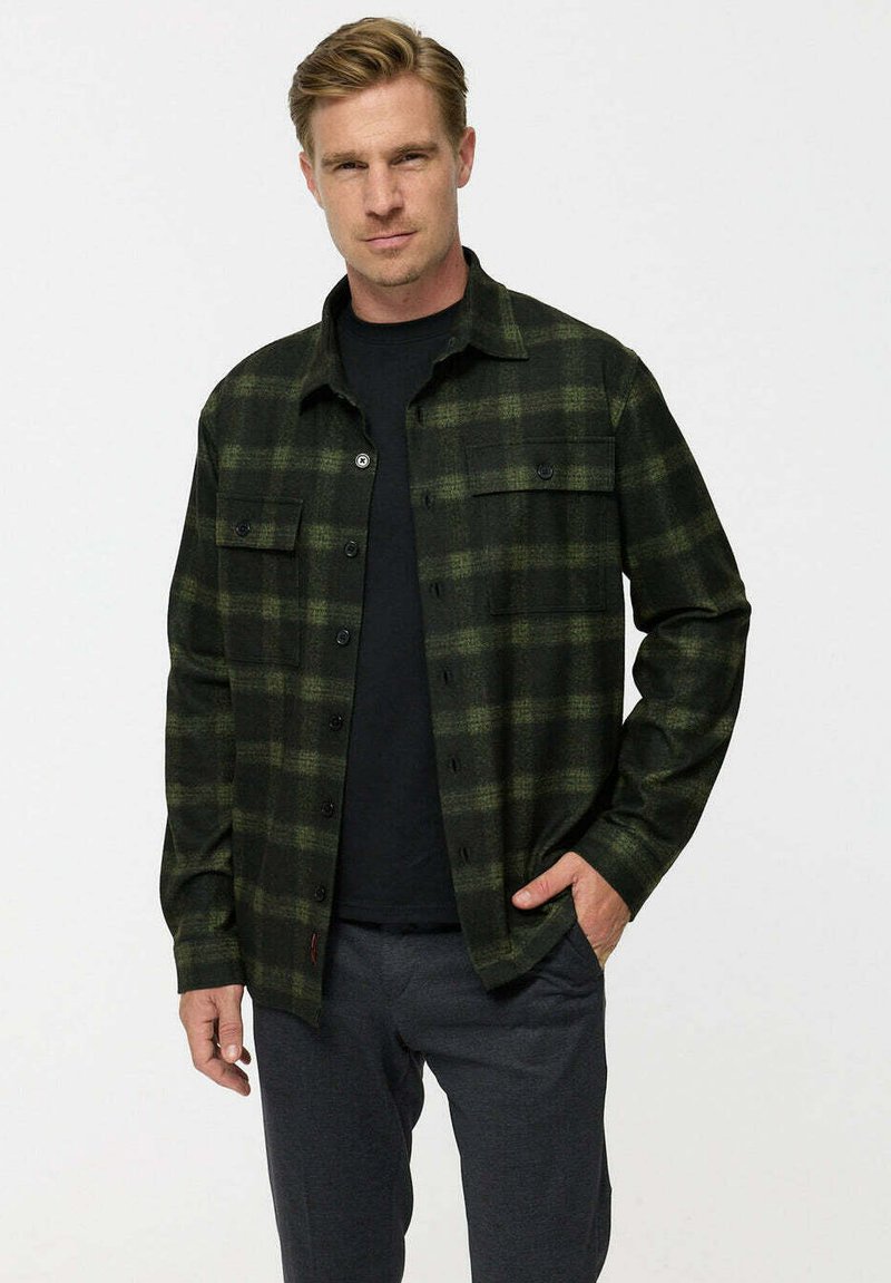 Green plaid flannel shirt with a button-up design, two chest pockets, and black buttons, worn over a black t-shirt. Soft texture.