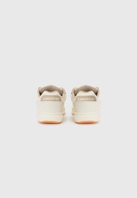 Tenisi bej din pânză cu un design low-top, având laturi texturate, tălpi contrastante de culoare deschisă și brandul "CONVERSE" pe călcâi.