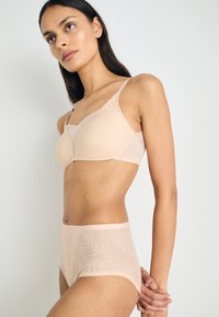 Nude bh og høyhøydet undertøy laget av gjennomsiktig materiale med bølgete mønster. Glatt tekstur og justerbare stropper på bh-en.