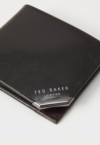 Crna kožna novčanica s glatkom teksturom, sadrži srebrnu akcentaciju u kutu i bijeli natpis "TED BAKER LONDON."