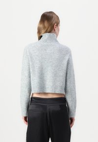 Pull cropped bleu clair en matière douce et texturée avec un col montant à côtes. Associé à un pantalon noir taille haute, laissant entrevoir un léger ventre.