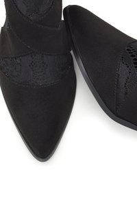 Melni potīšu zābaki ar smailu purngalu, veidoti no zamša un mežģīnēm, ar krusteniskajām mežģīnēm priekšpusē un platu zoli.