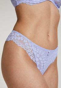 Lila kanten strings met scalloped randen en een contrasterende gladde tailleband. Voorzien van decoratieve knopen op de achterkant voor extra detail.